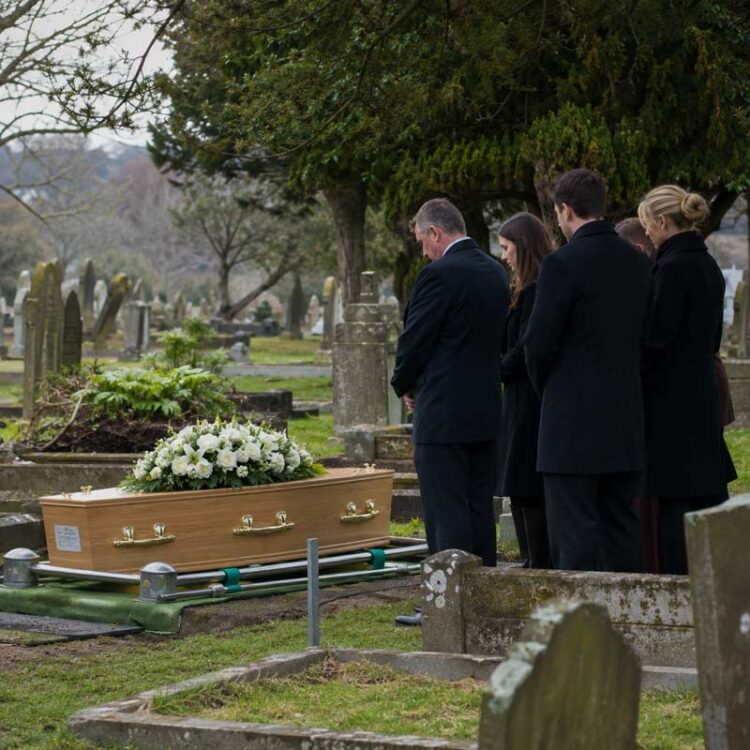 Family members gathered beside a wooden coffin during a burial service in a cemetery.