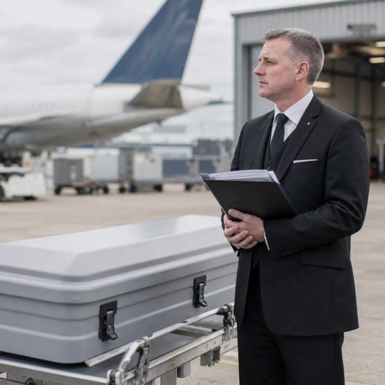 Funeral director holding repatriation documents beside an airline transport case at an airport.
